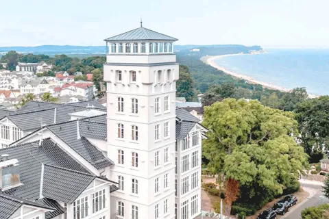 Aktuelle Aussenansicht des Vju Hotels auf Rügen mit dem prominentem Turm im Fokus und der Ostsee im Hintergrund.