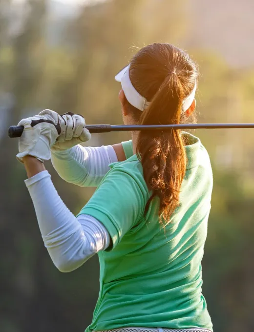 Frau beim Golfschwung auf einem grünen Golfplatz, konzentrierte Haltung und sonnige Umgebung.