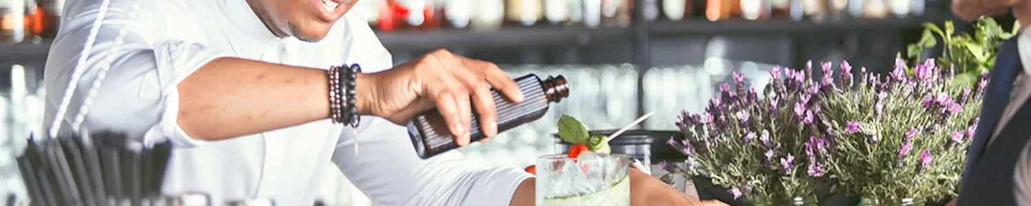 Ein Barkeeper kreiert an der Bar einen Cocktail. Der Kellner steht schon bereit.