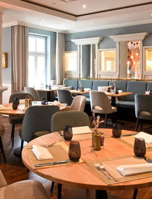 Blick in das maritime Restaurant Küstensilber mit hellen Stühlen und Bänlen, Holzdekor und eingedeckten Tischen im Vju Hotel auf Rügen.