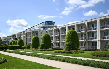 Außenansicht des Hotel Kaiserhof in Heringsdorf mit Balkonen, gepflegten Grünflächen und einem gläsernen Aufbau.