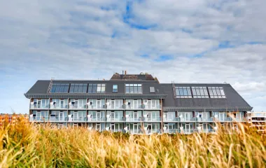 Außenansicht des Wyn Strandhotels auf Sylt, umgeben von Gräsern unter leicht bedecktem Himmel.