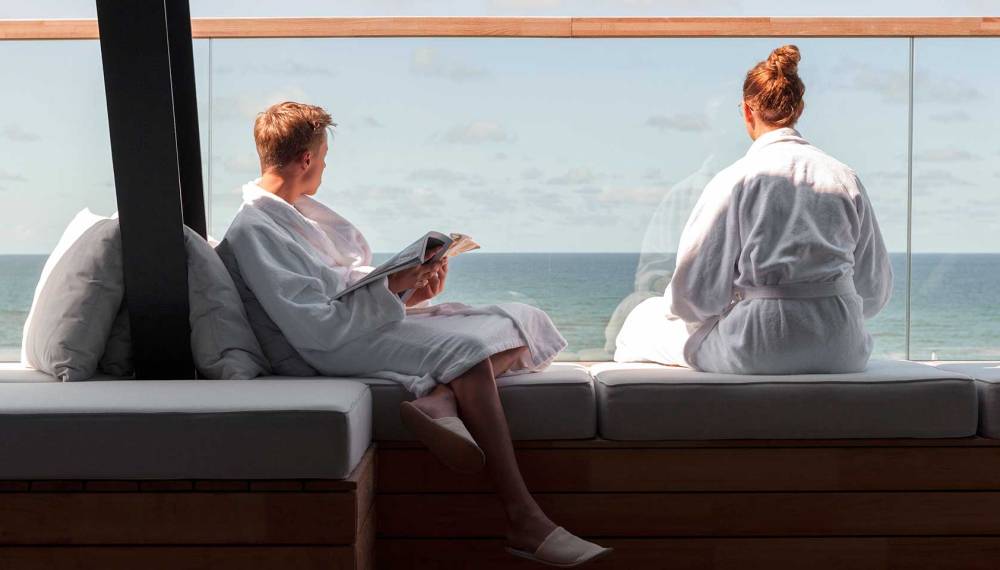 Ein Paar sitzt entspannt in der Spa.Lounge des Wyn. Strandhotels Sylt mit Blick auf die Nordsee.