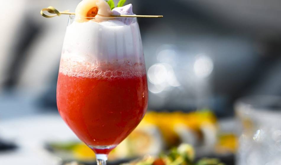 Cocktail mit rotem Saft und Schaumkrone, garniert mit Lychee und Minzblatt auf einem Holzstäbchen im #herrhoshi in Ahrenshoop.