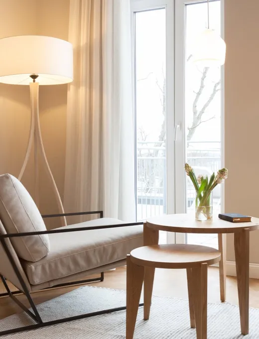 Moderne Sitzecke im Vju Hotel Rügen mit hellem Sessel, Holzbeistelltisch und großer Fensterfront.
