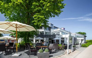 Außenansicht des Künstlerquartier Seezeichen Hotels in Ahrenshoop mit Stühlen und Sonnenschirmen unter blauem Himmel.