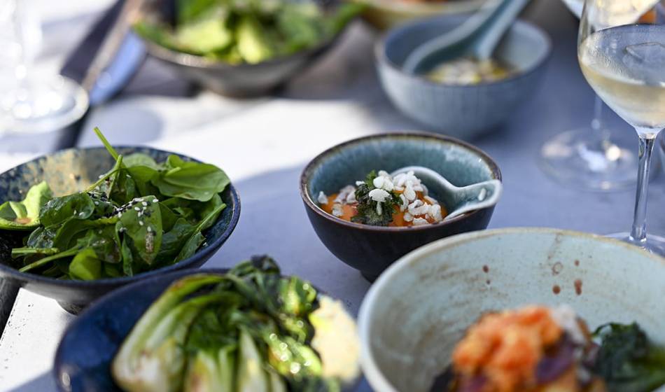 Eine Auswahl an frischen vegetarischen Speisen in Schalen angerichtet, mit grünem Blattgemüse und verlockenden Details.