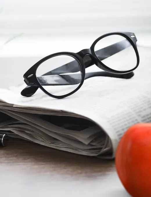 Nahaufnahme einer Brille, die auf einer Zeitung liegt, mit einem orangefarbenen Detail im Bild.