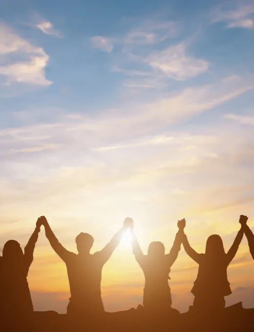 Personen stehen Hand in Hand und heben ihre Arme vor einem farbenprächtigen Sonnenuntergang.