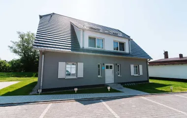 Strandvilla Seezeichen in Ahrenshoop mit weißen Fensterläden, großem Dach und gepflegtem Garten.