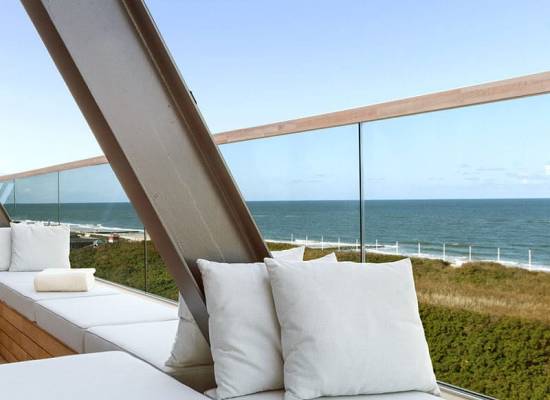 Moderne Terrasse des Wyn Strandhotels Sylt mit weißen Sitzpolstern und Blick auf das Meer und Dünen.