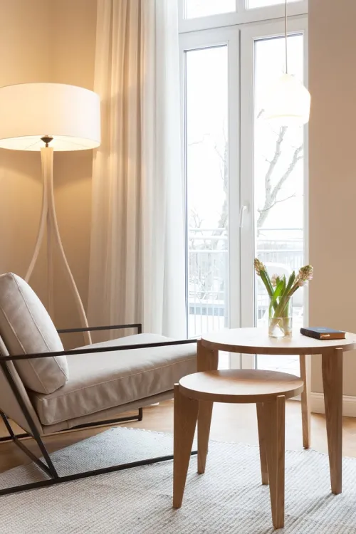 Moderne Sitzecke im Vju Hotel Rügen mit hellem Sessel, Holzbeistelltisch und großer Fensterfront.