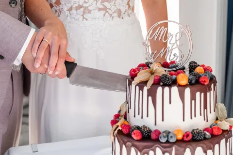 Brautpaar schneidet üppige Hochzeitstorte mit Beerenverzierung an.