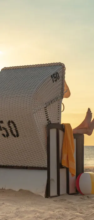 Person entspannt im Strandkorb am Ostseestrand bei Sonnenuntergang im Sommerurlaub im Vju Hotel auf Rügen.
