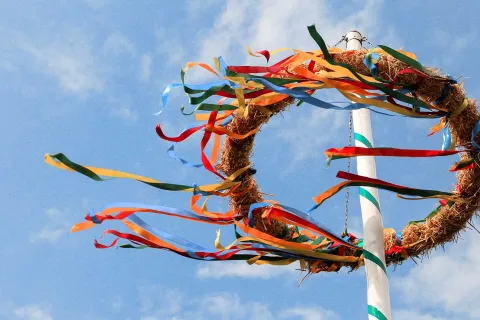 Ein weiß-grüner Maibaum mit einer Krone, deren bunte Bänder sich im Wind bewegen.