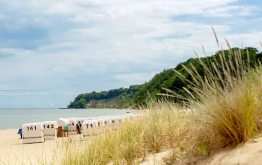 Ein ruhiger Ostseestrand auf Rügen mit Strandkörben, umgeben von Dünen und einer grünen Küstenlandschaft, die zum Entspannen einlädt.
