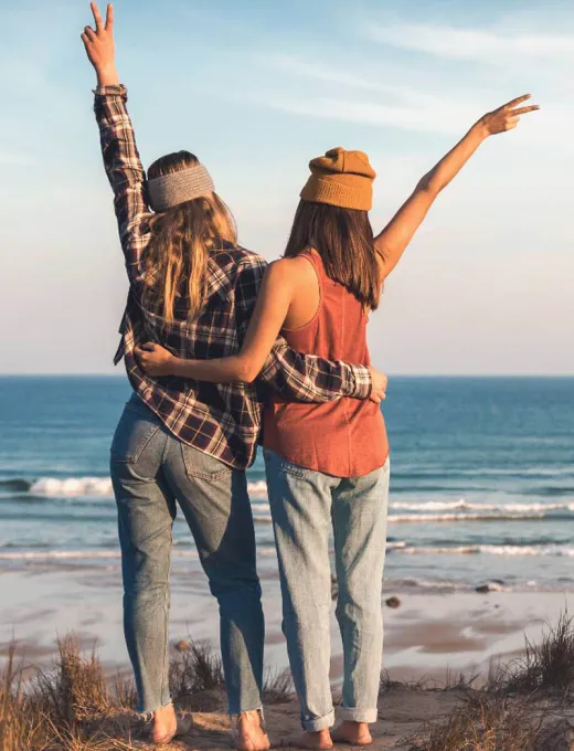 Rückansicht von zwei Frauen, die sich umarmen und den Ausblick auf das Meer genießen.