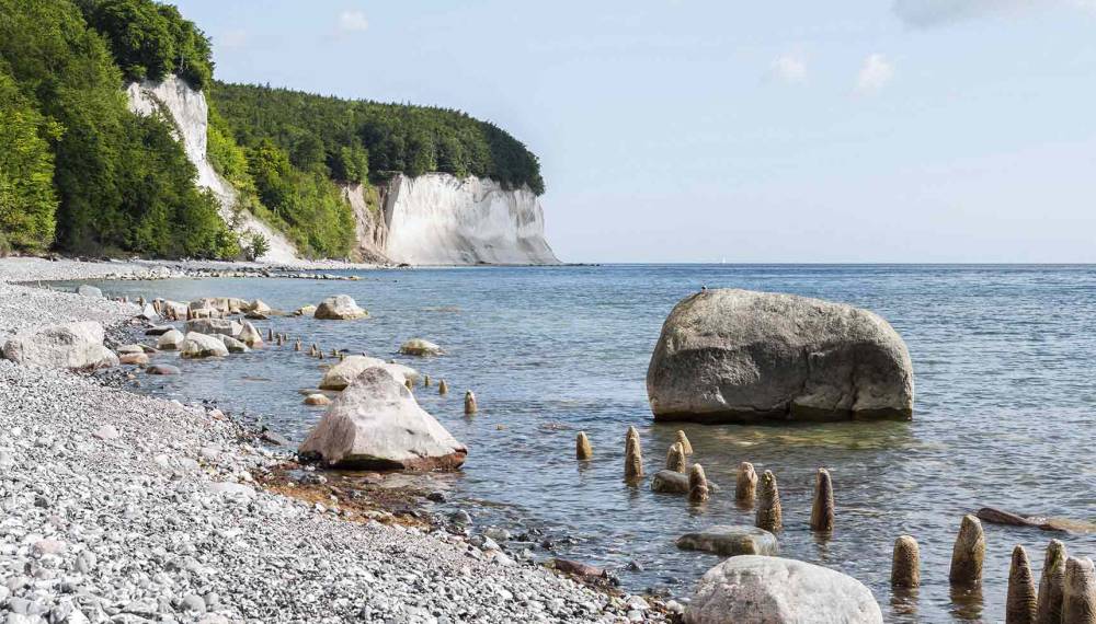 Blick auf die Kreideküste am Königsstuhl auf Rügen mit großem Findling, Kiesstrand und der ruhigen Ostsee.