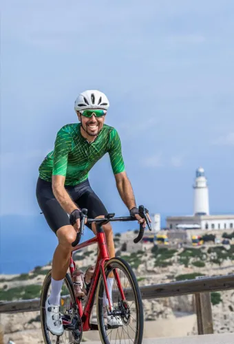 Radfahrer auf einer sonnigen Küstenstraße auf Mallorca mit Meer und Bergen im Hintergrund