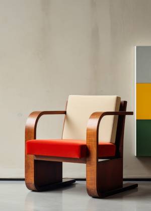 Detailaufnahme eines Stuhls aus der Bauhaus-Ära, rotes Polster und Holzrahmen, vor moderner Wandkunst im Museum in Weimar