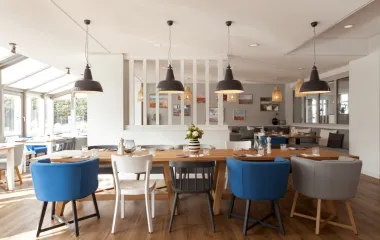 Helles Restaurant mit Holztisch, blauen und grauen Sesseln, Pendelleuchten und Blumendeko im Wyn. Strandhotel Sylt