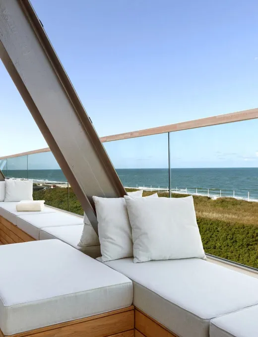 Moderne Terrasse des Wyn Strandhotels Sylt mit weißen Sitzpolstern und Blick auf das Meer und Dünen.