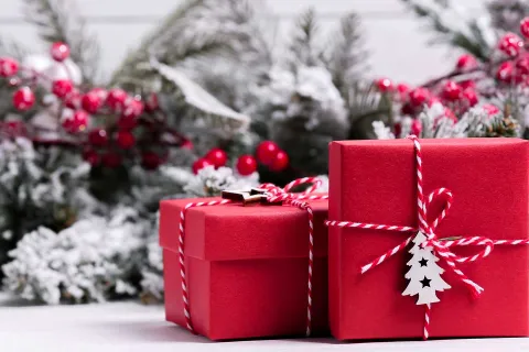 Rote Weihnachtsgeschenke vor vor Weihnachtsdeko aus Tannenzweigen und roten Beeren.