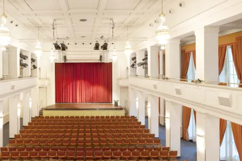 Innenansicht des Kaiserbädersaals in Heringsdorf mit Bühne, roten Theatervorhängen, Sitzreihen und umlaufender Galerie