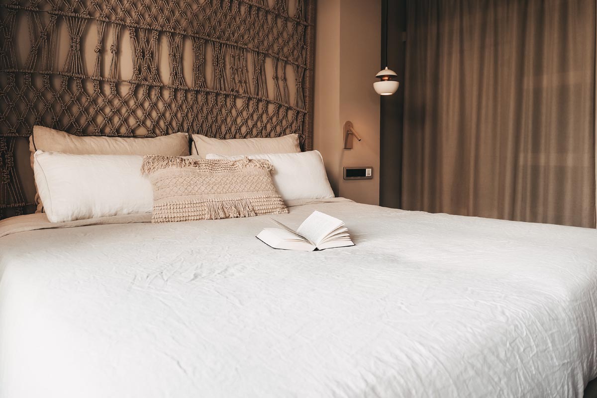 Cómoda cama de matrimonio en la habitación doble Puerto del Hotel Barefoot Mallorca con cabecero decorativo y libro abierto.