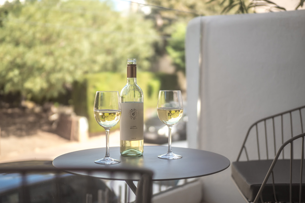 Botella de vino blanco con dos copas llenas en una mesa en la terraza de la habitación doble Puerto en el Barefoot Hotel Mallorca