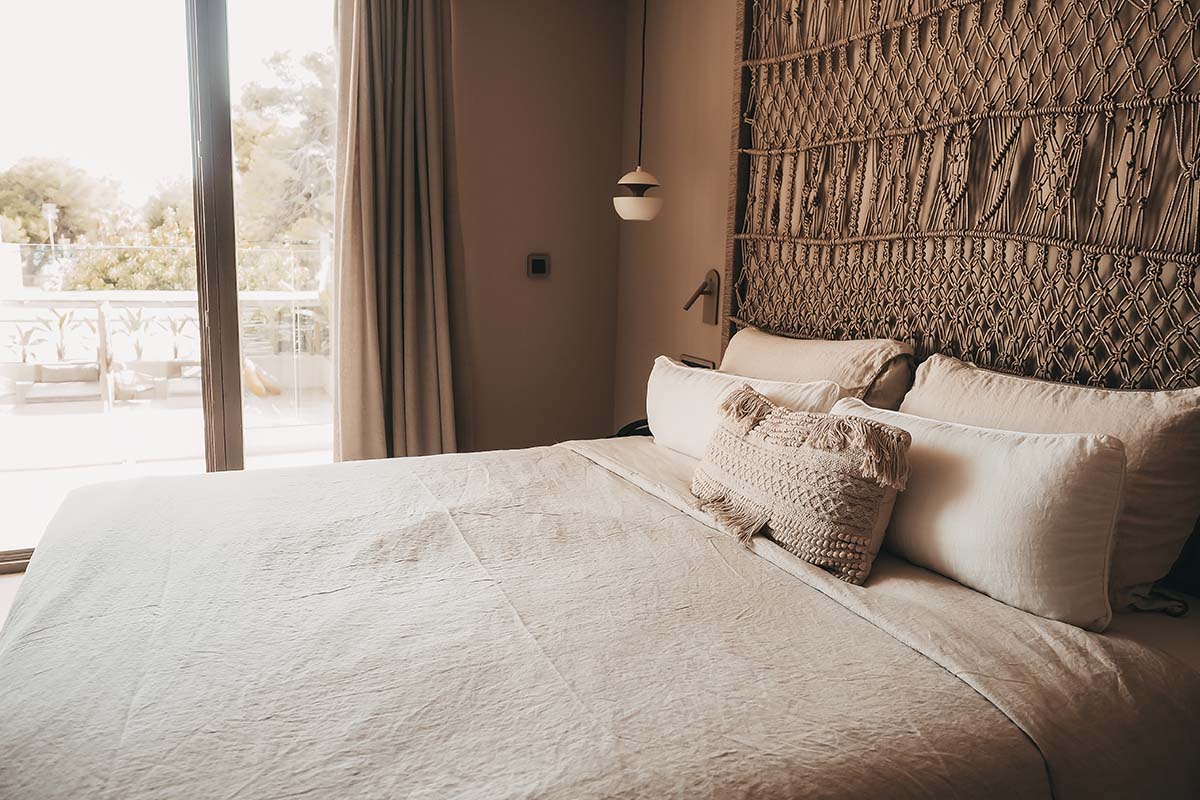 Amplia cama doble en la Habitación Doble Deluxe Oasis del Hotel Barefoot Mallorca con cabecero decorativo, suaves almohadas y vistas al balcón.