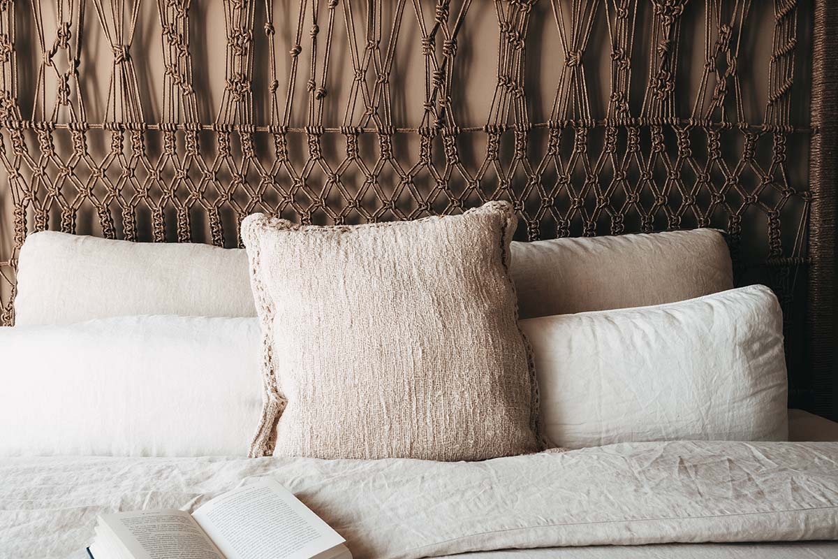 Cojines decorativos y un libro abierto sobre una acogedora cama de matrimonio en la habitación doble Oasis del hotel Barefoot de Mallorca.