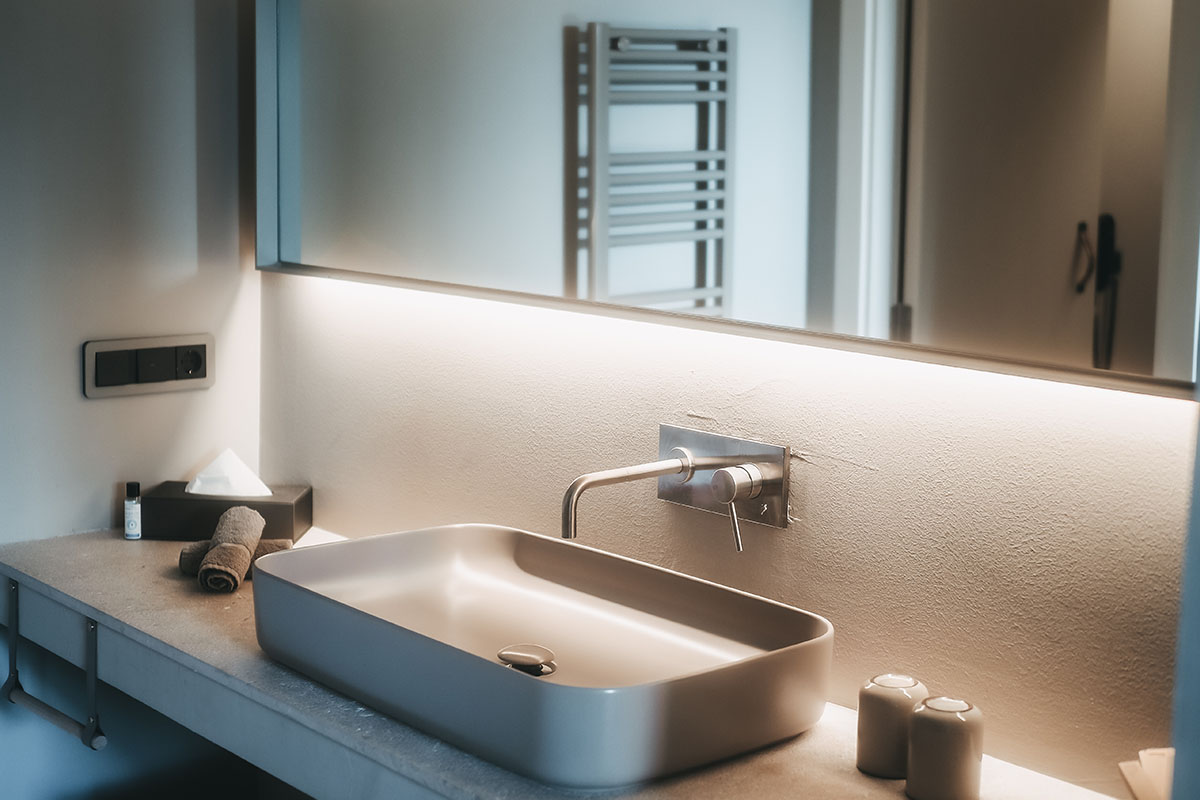 Lavabo en la habitación doble Oasis del Hotel Pies Descalzos de Mallorca con un diseño moderno, un gran espejo y una iluminación elegante.
