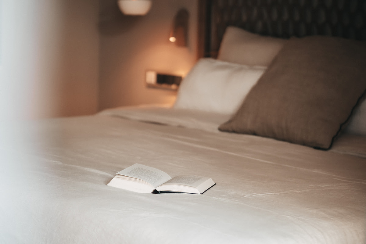 Schlafbereich im Zimmer Pino des Barefoot Hotel Mallorca mit aufgeschlagenem Buch auf einem großen Bett und gemütlichen Kissen.
