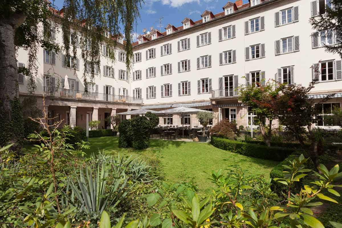 The garden of the Hotel Elephant Weimar with lush greenery and the imposing hotel building in classical architecture.