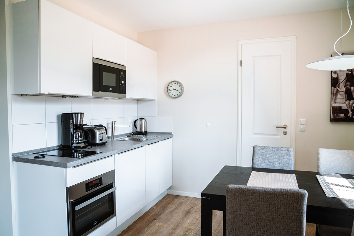 Voll ausgestattete Küchenzeile der Ferienwohnung Dünenpark des Hotels Künstlerquartier Seezeichen mit Essplatz und Seeblick.
