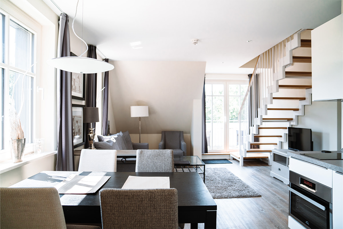 Heller Wohnbereich mit Esstisch, Sofa und Treppe in der Ferienwohnung Dünenpark, Teil des Hotels Künstlerquartier Seezeichen.