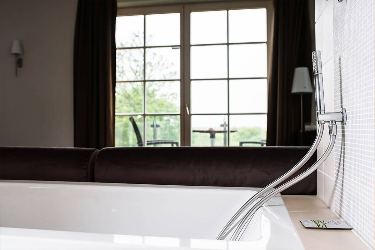 Freistehende Badewanne vor einer großen Balkontür mit Blick auf die Natur in der Deluxe Suite im Hotel Künstlerquartier Seezeichen.