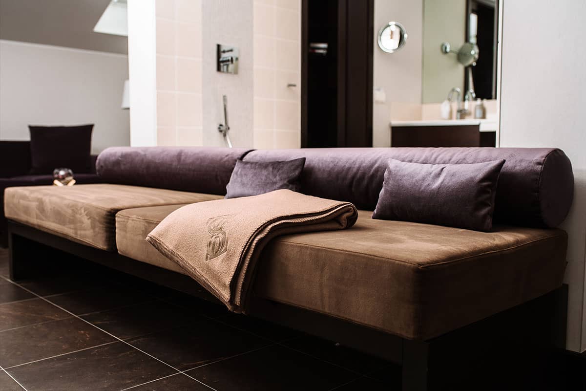 Bequeme Polsterbank mit dekorativer Decke im modernen Badezimmer der Deluxe Suite im Hotel Künstlerquartier Seezeichen.