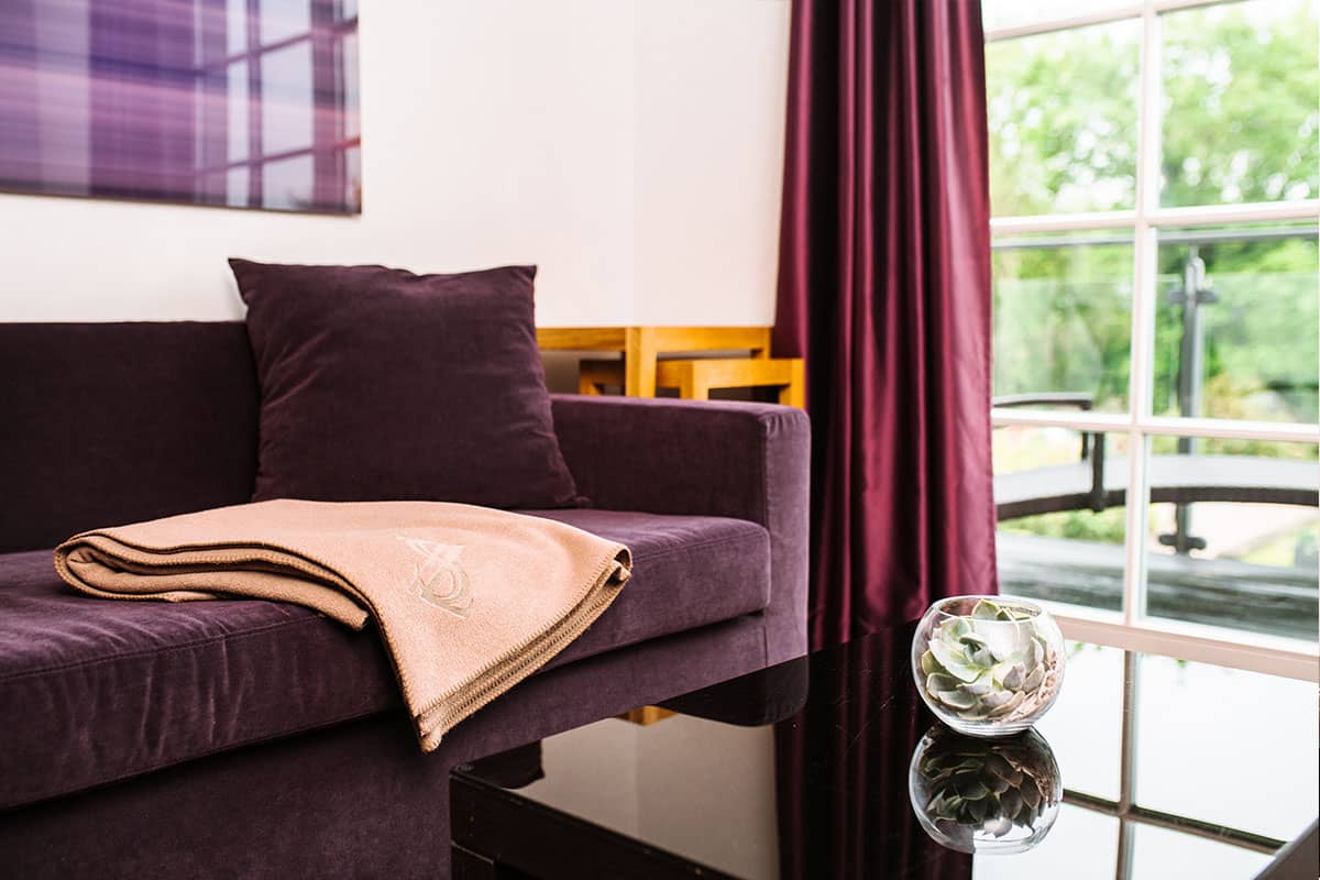 Nahaufnahme einer gemütlichen Couch mit weichen Kissen und einer Decke in der Deluxe Suite des Hotel Künstlerquartier Seezeichen.