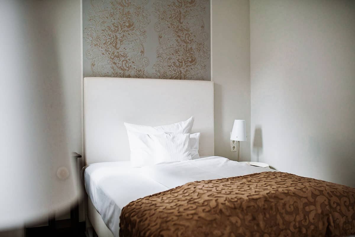 Stilvolles Einzelbett mit eleganter Bettwäsche im Einzelzimmer des Hotel Künstlerquartier Seezeichen.