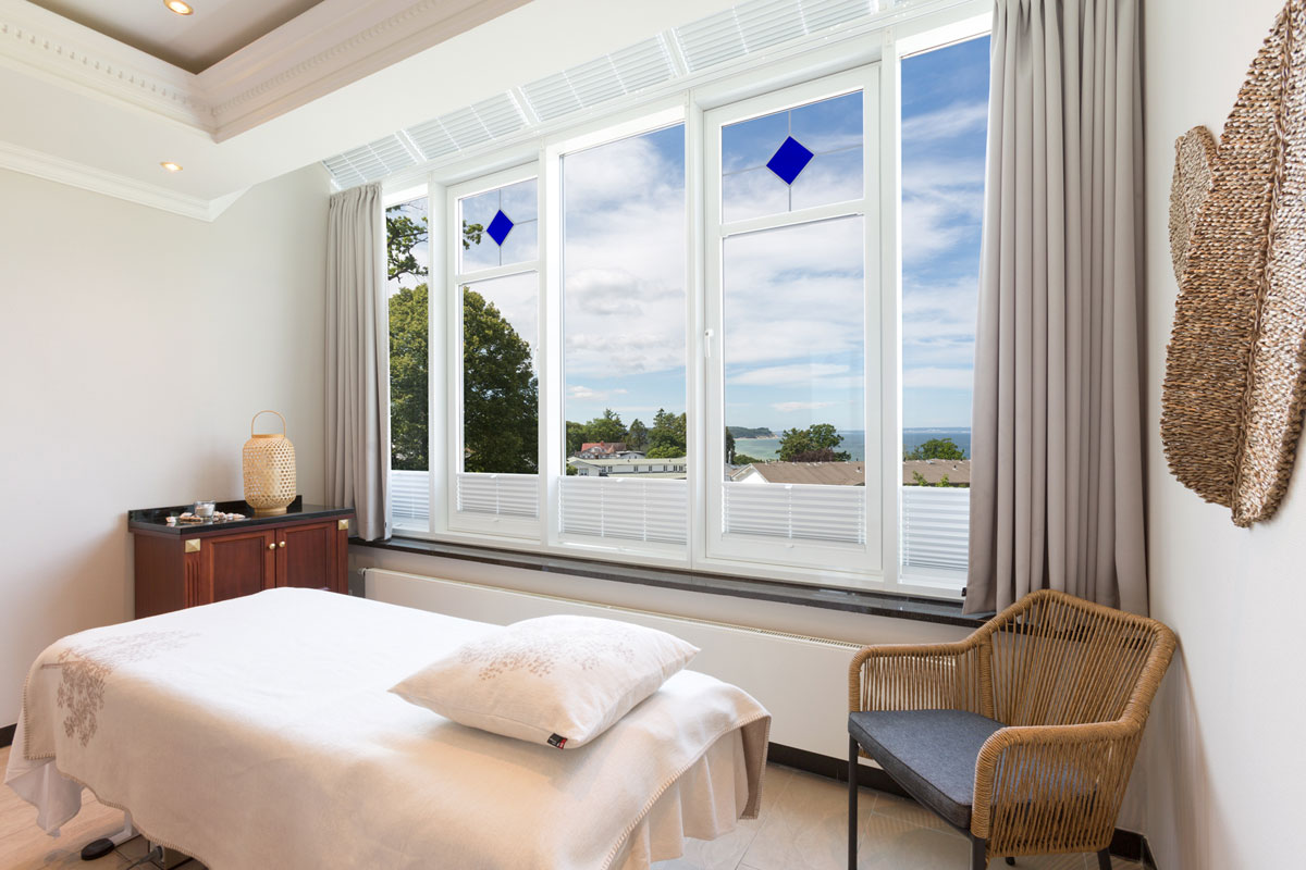 Heller Massageraum mit großer Fensterfront, bequemer Liege und Blick auf das Meer im Wellnessbereich des Vju Hotels.