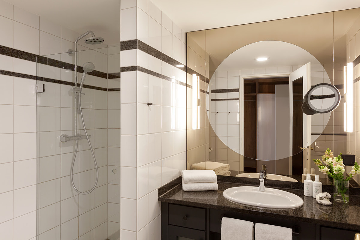 Modernes Badezimmer mit Spiegelwand, Waschtisch, Handtüchern und Dusche im Doppelzimmer des Vju Hotels.