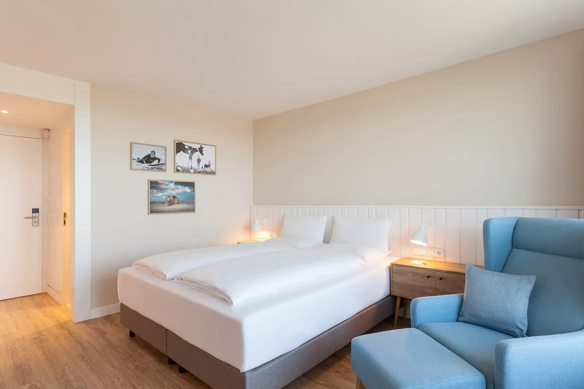 Helles Hotelzimmer Muschelsucher im Wyn. Strandhotel auf Sylt mit großzügigem Bett und gemütlicher Beleuchtung.