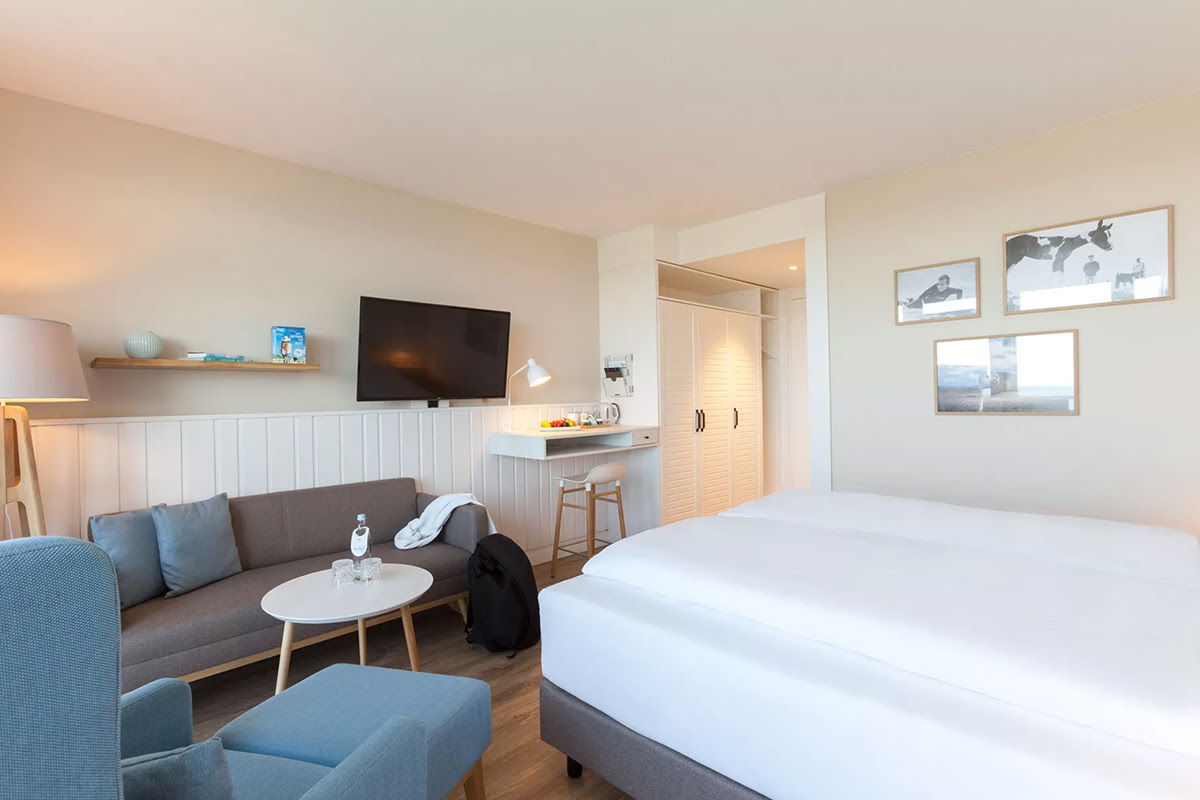 Helles und modernes Muschelsucher-Zimmer mit großem Bett und gemütlicher Sitzecke im Wyn. Strandhotel auf Sylt.